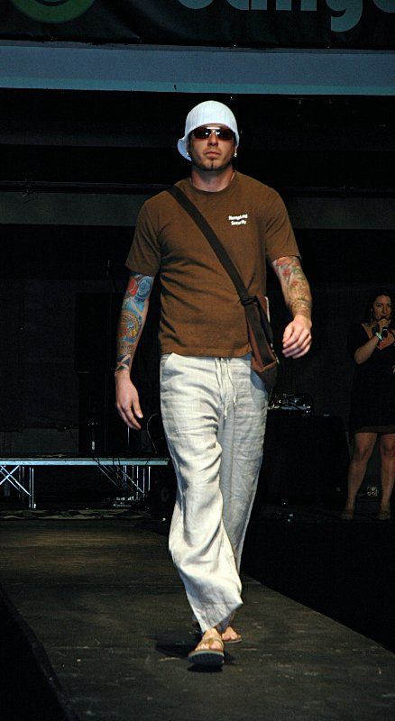 A man in a brown shirt and white pants is walking down a runway.