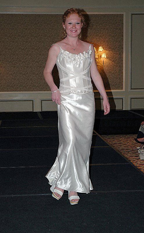 A woman in a white dress is walking down a runway