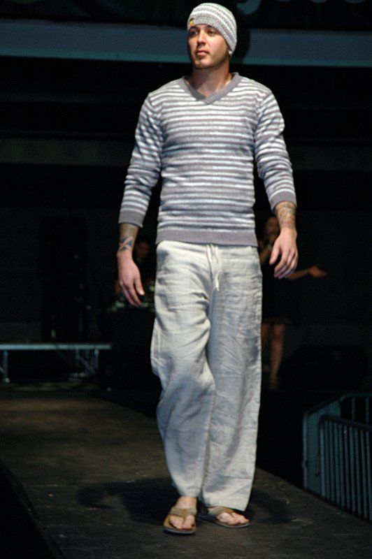 A man wearing a striped sweater and white pants walks down a runway