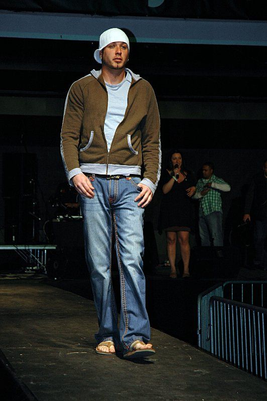 A man wearing a hat is walking down a runway