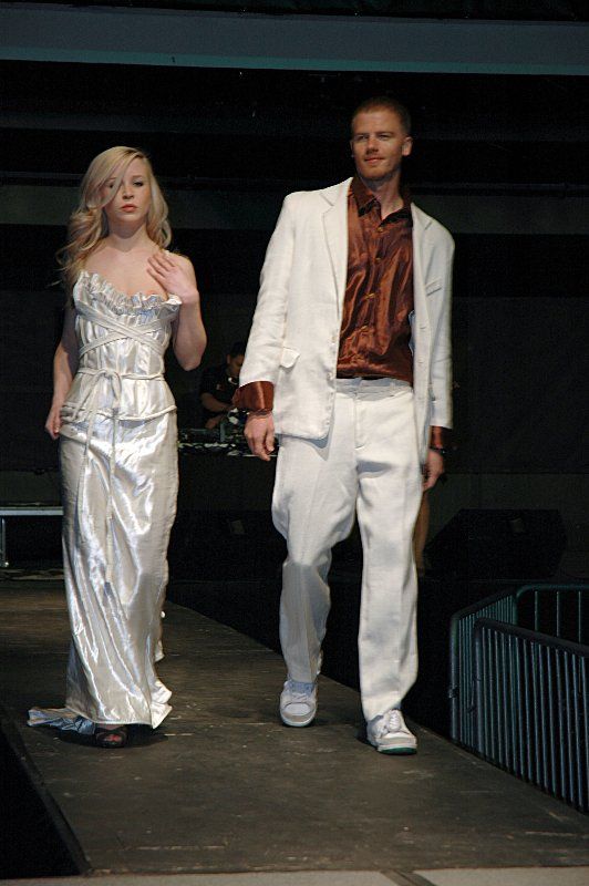 A woman in a white dress and a man in a white suit are walking down a runway.