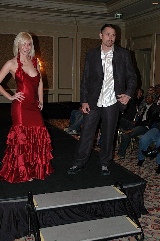A man in a suit and a woman in a red dress are walking down a runway
