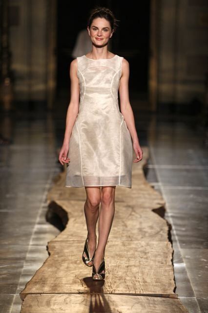 A woman is walking down a runway wearing a white dress.