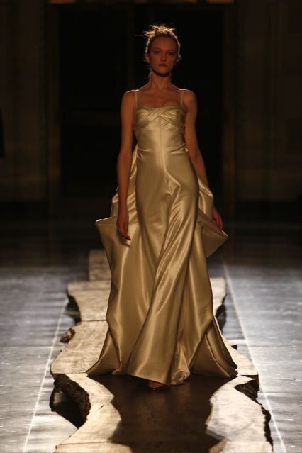 A woman in a white dress is walking down a runway