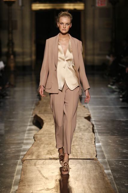 A model walks down the runway at a fashion show wearing a tan suit