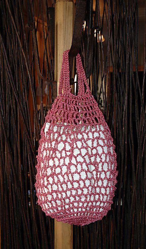 A pink crocheted bag is hanging from a wooden pole.