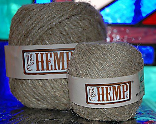Two balls of hemp yarn sit on a table in front of a stained glass window