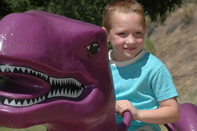 A young boy is riding on the back of a purple dinosaur