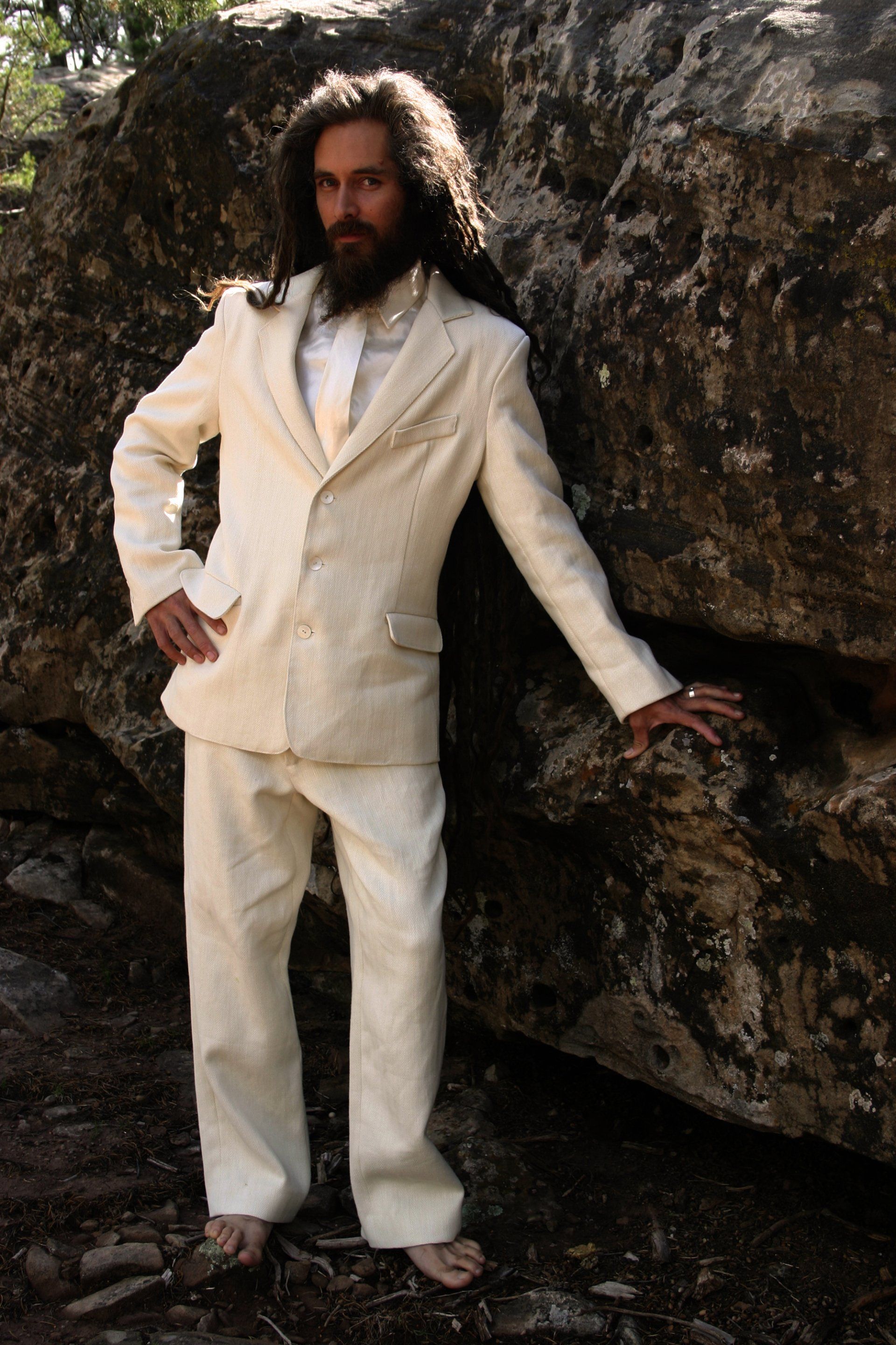 A man with long hair and a beard is wearing a white suit