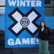 A woman is standing in front of a Winter X Games sign.