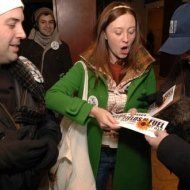 A woman in a green coat is talking to a man in a blue hat.