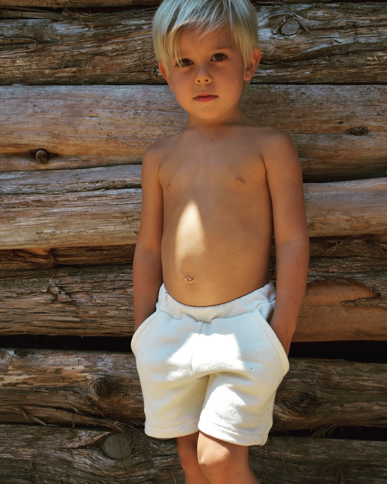 little kid wearing hemp shorts standing by log cabin