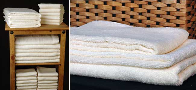 A stack of white towels on a wooden shelf next to a stack of white towels on a bed.