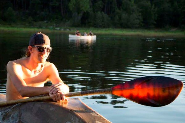 A shirtless man is paddling a canoe on a lake