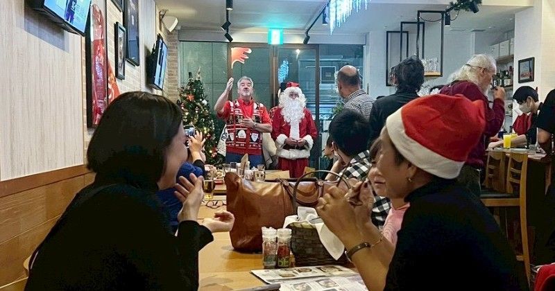 People in restaurant celebrate Christmas, watching Santa. Christmas decorations, people smiling.