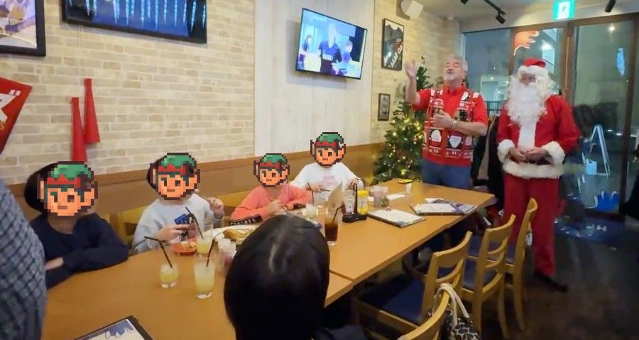 People at a table with Santa and another man giving a speech at a restaurant during Christmas.