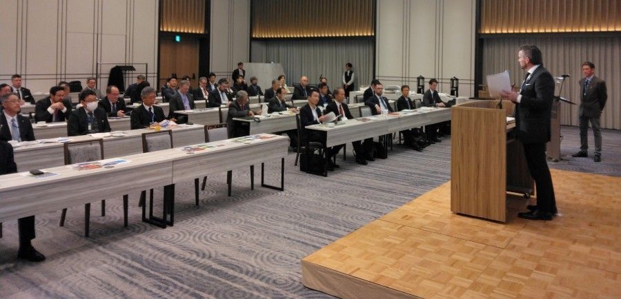 A man is giving a speech in front of a large group of people in a conference room.