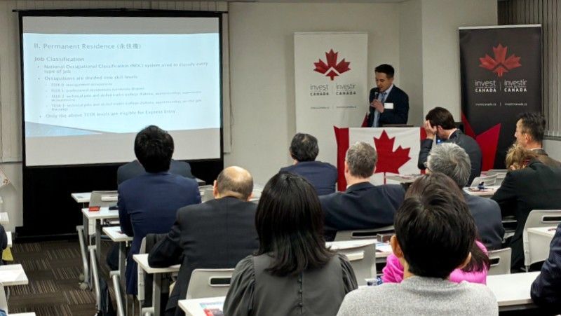 Yuji Matson giving presentation at a seminar with audience. Canadian flag and branding visible.