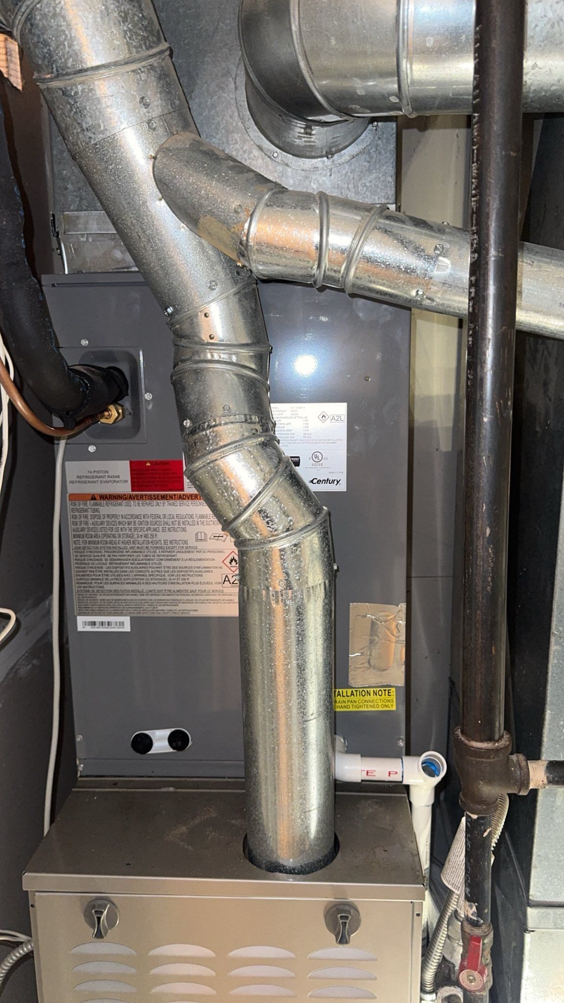 Furnace with metal ductwork and pipes in a utility room.