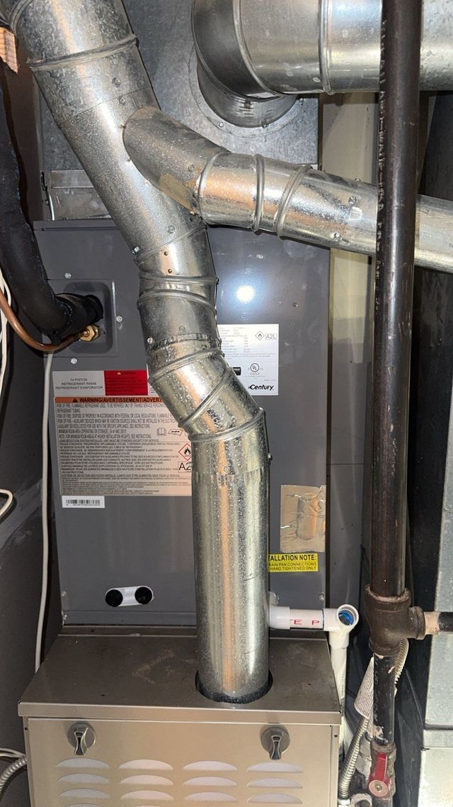 Furnace with metal ductwork and pipes in a utility room.