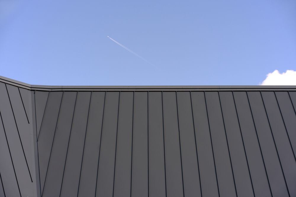 A Plane is Flying in the Sky Above a Gray Roof — Rhythm Roofing in Woolgoolga, NSW