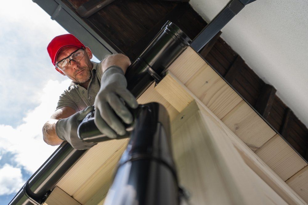 A Man is Working on a Gutter on the Roof of a House — Rhythm Roofing in Byron Bay, NSW