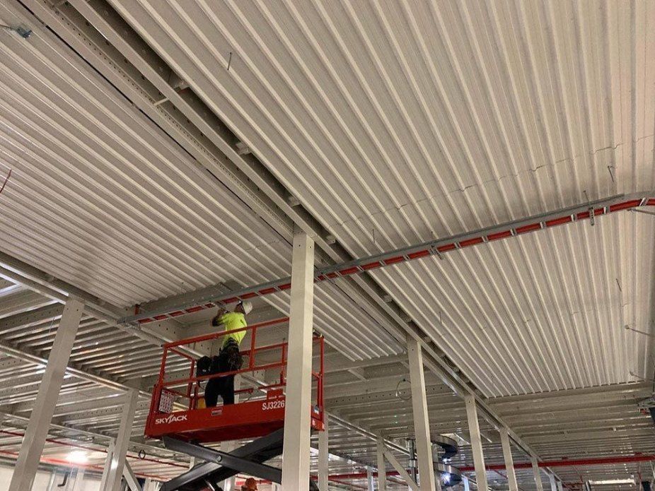 A Man is Standing on a Scissor Lift Working on the Ceiling of a Building — Rhythm Roofing in North Boambee Valley, NSW