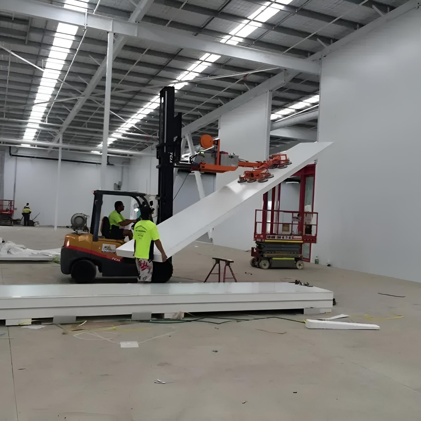A Man in a Yellow Shirt is Standing Next to a Forklift in a Large Warehouse — Rhythm Roofing in North Boambee Valley, NSW