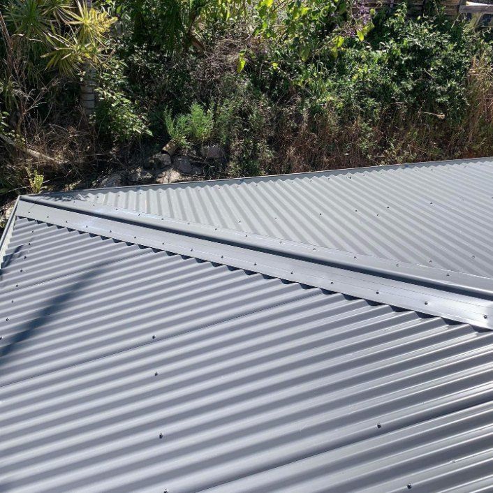 A Close Up of a Gray Corrugated Metal Roof With Trees in the Background — Rhythm Roofing in Penrith, NSW