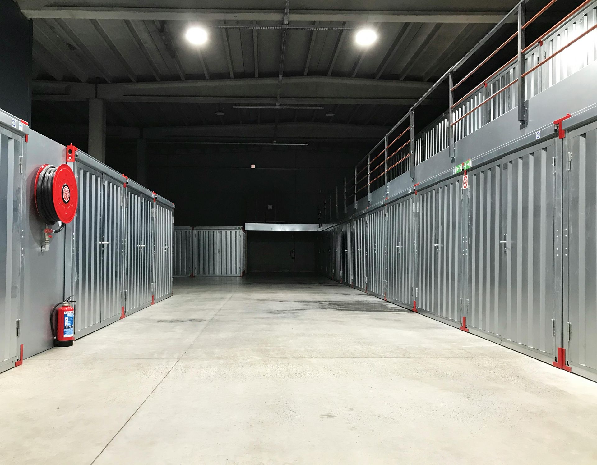 Pasillo industrial vacío con unidades de almacenamiento grises y luces en el techo.
