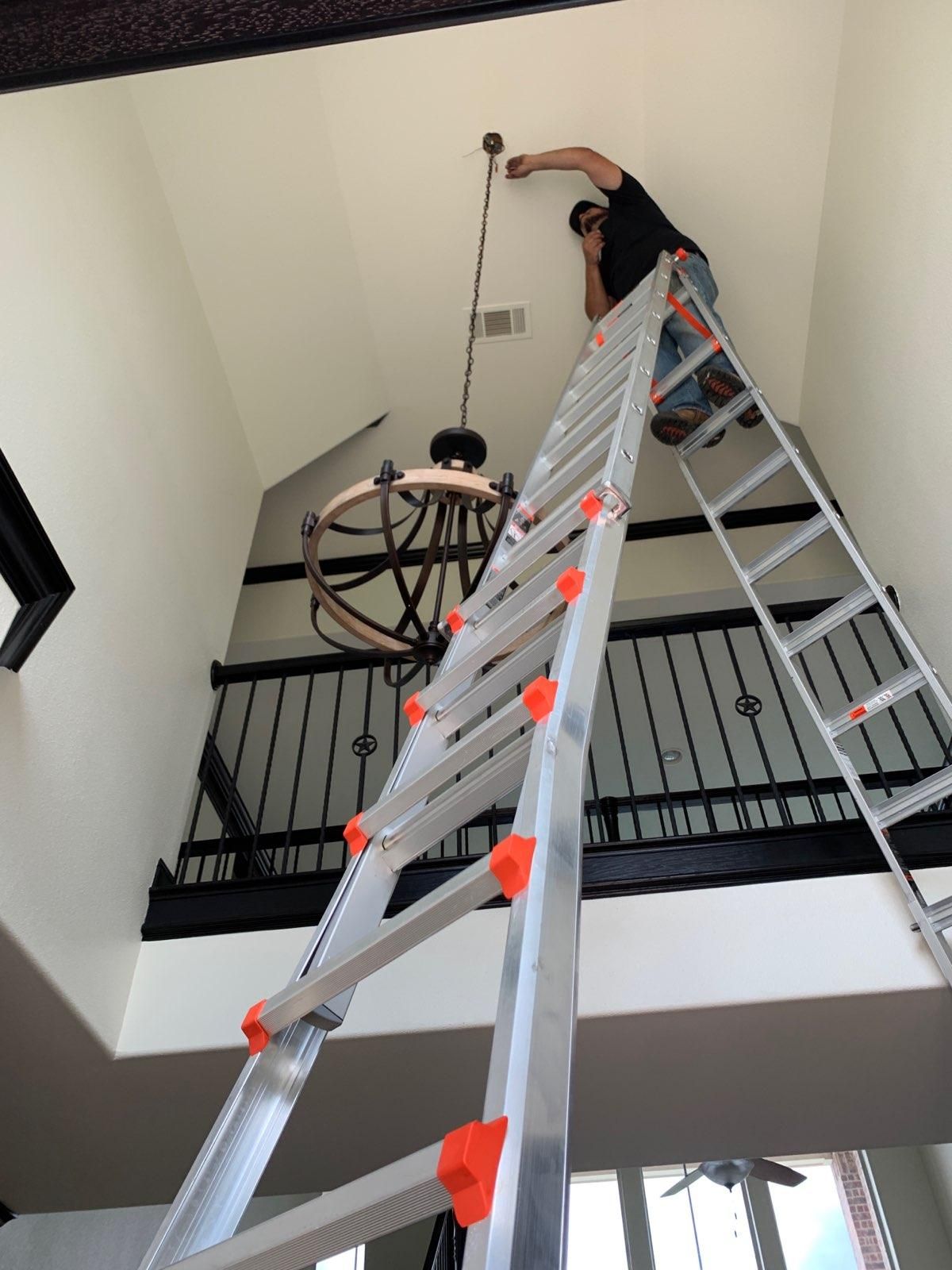 A man is standing on a ladder working on a chandelier.