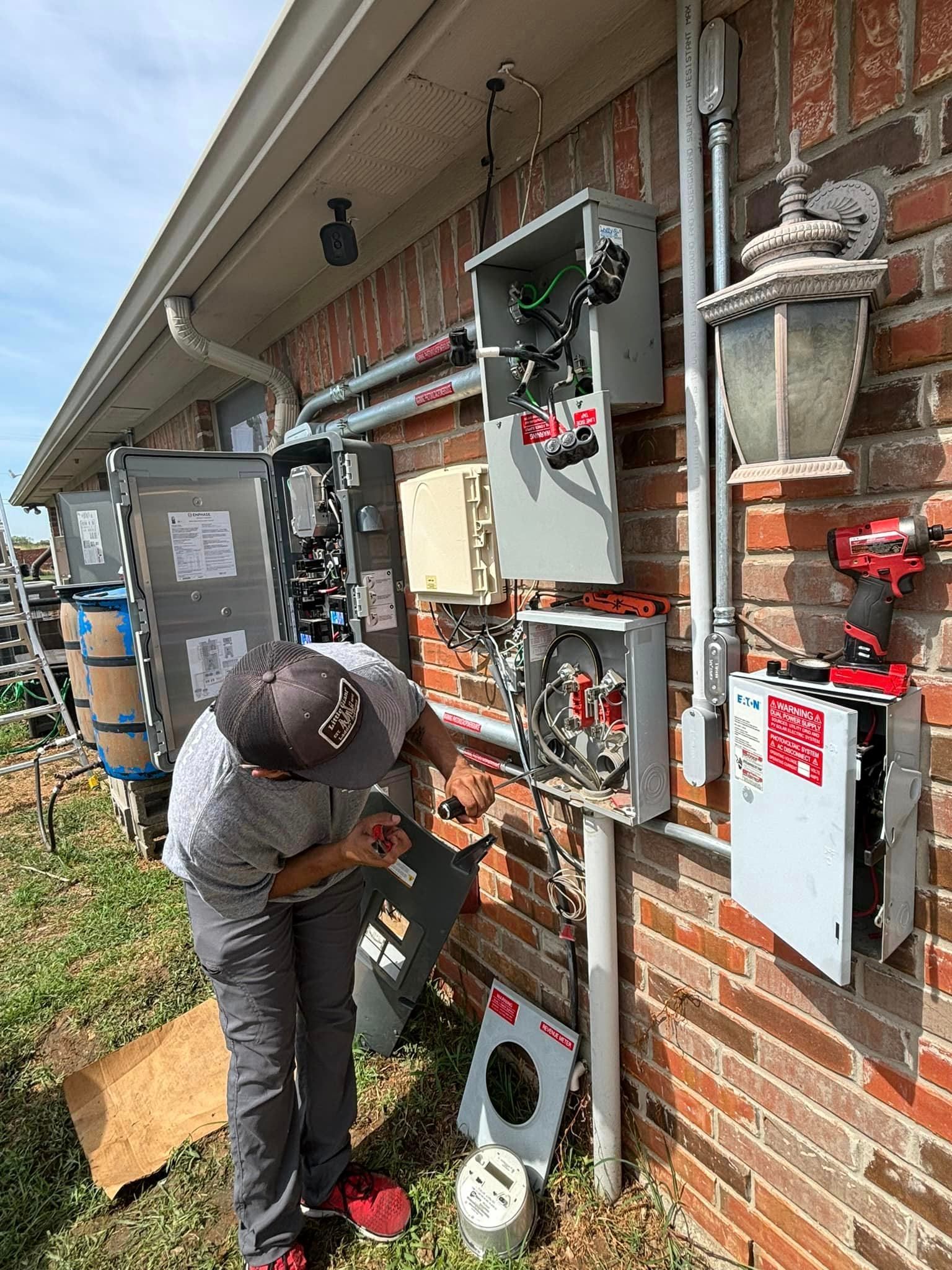 A man is working on a electrical box on the side of a brick building.