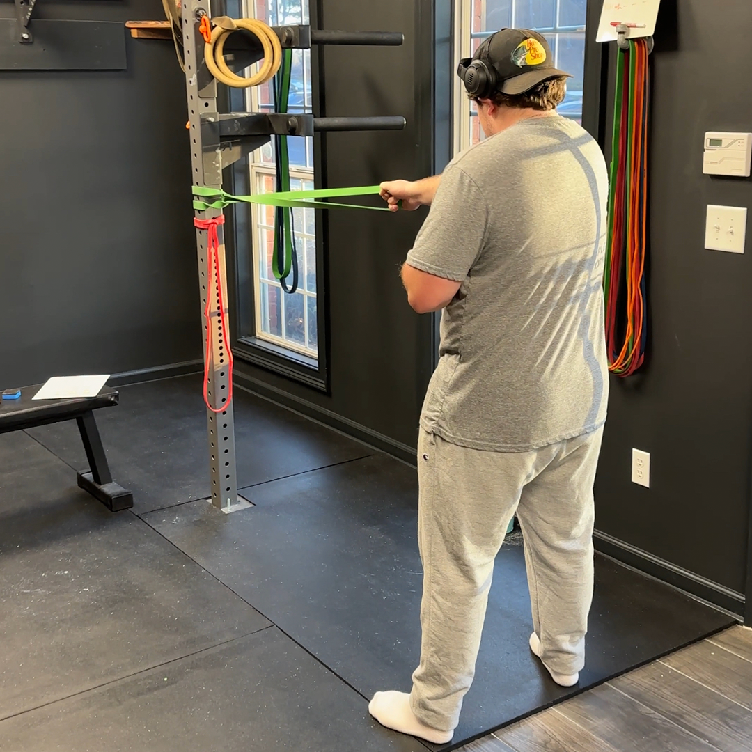 A man is standing in a gym holding a green resistance band