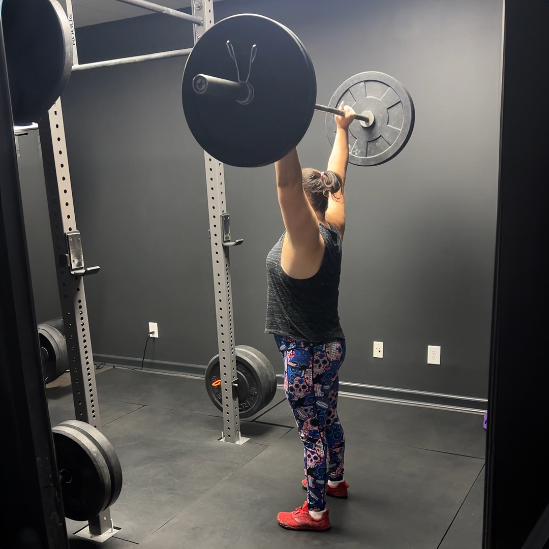 A woman is lifting a barbell over her head in a gym.