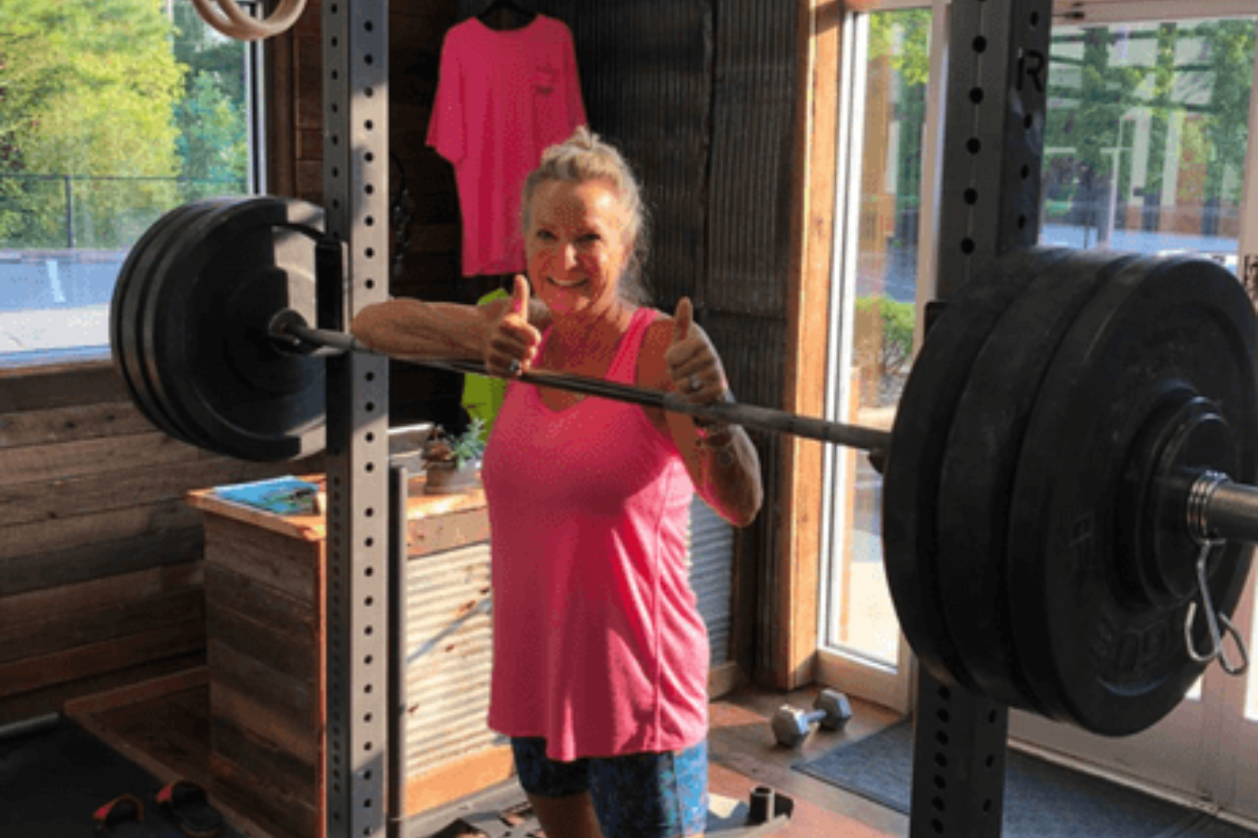 a woman is lifting a barbell in a gym and giving a thumbs up .