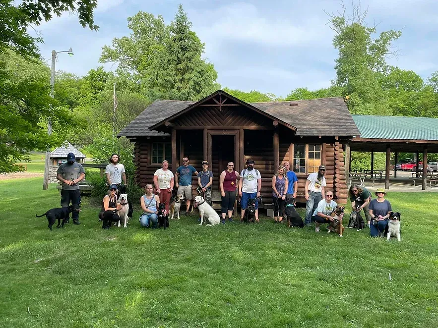 A group of people and their dogs are posing for a picture in front of a log cabin.