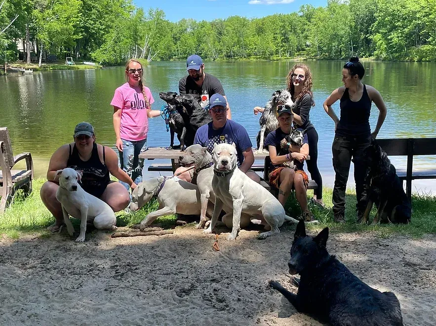 A group of people and their dogs are posing for a picture in front of a lake.