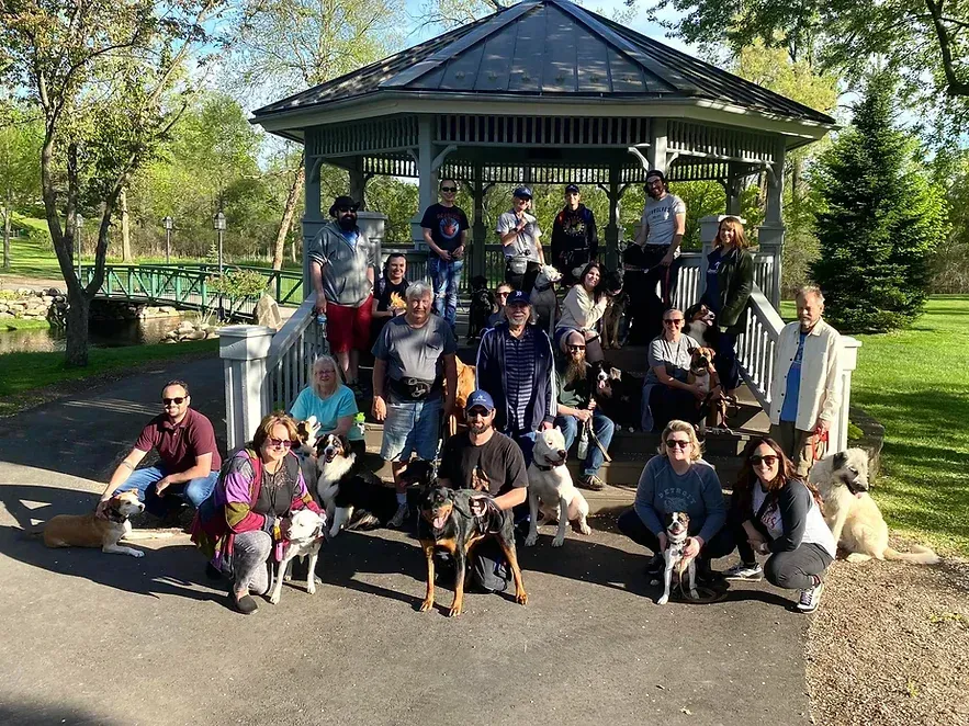 A group of people and their dogs are posing for a picture in front of a gazebo.