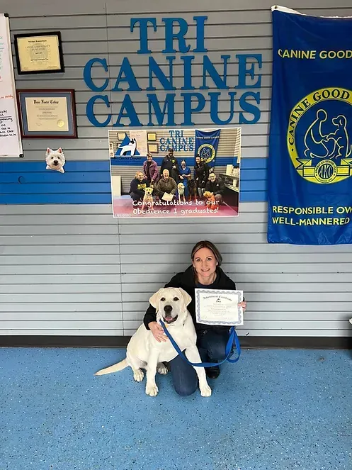 A woman is kneeling next to a dog in front of a sign that says tri canine campus.