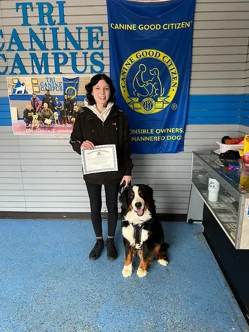 A girl is standing next to a dog in front of a tri canine campus banner.