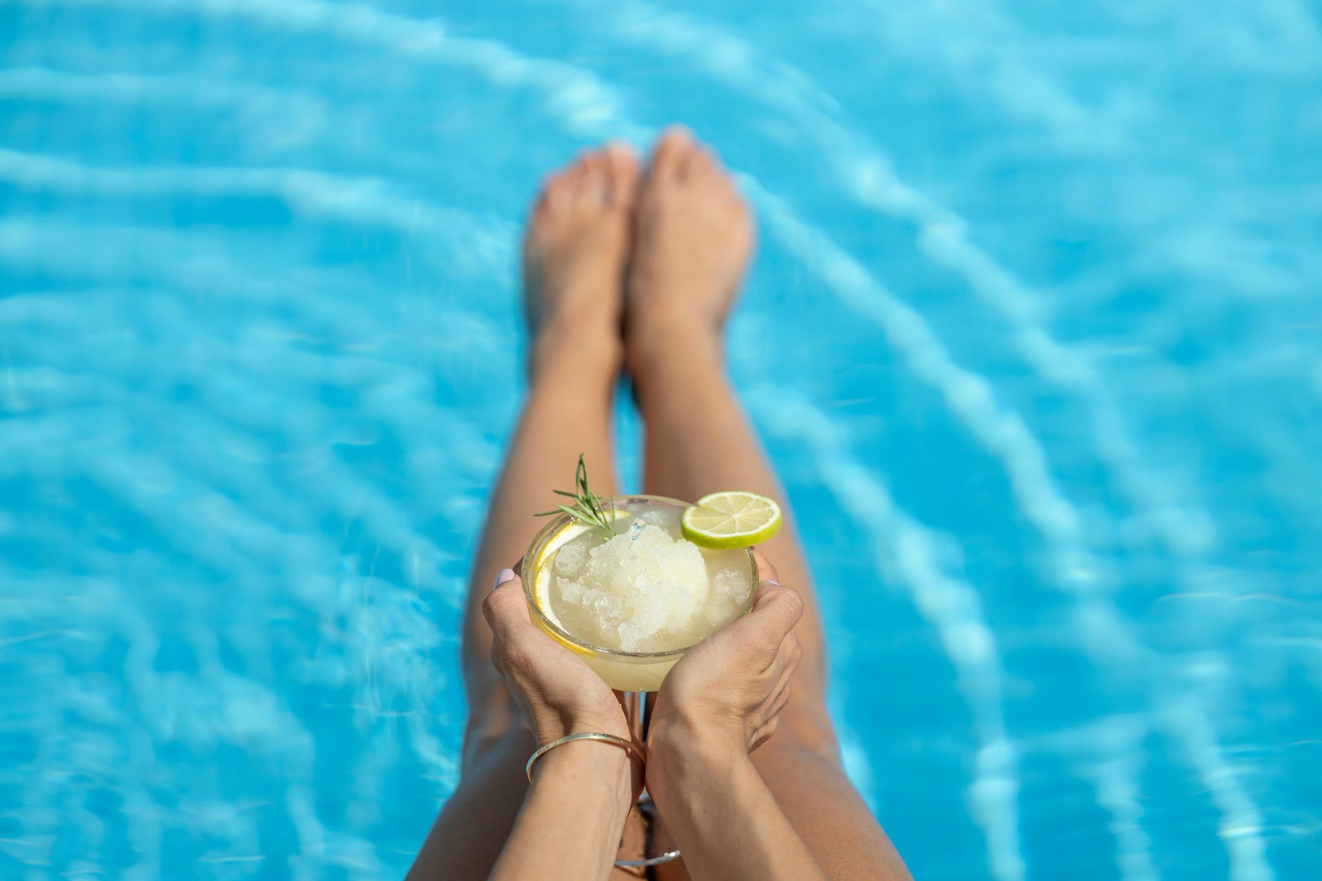 A woman is sitting in a swimming pool holding a drink in her hands.