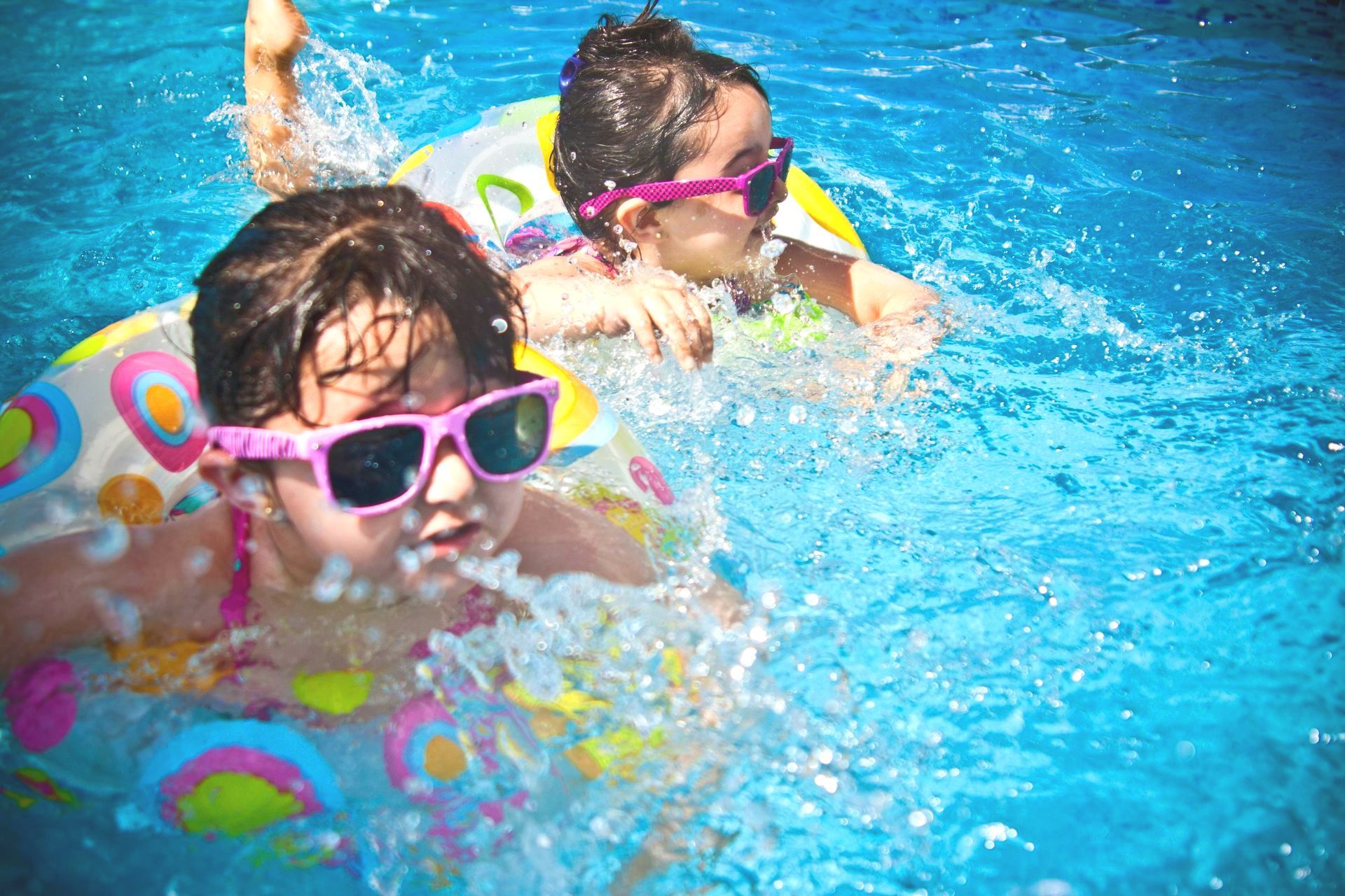Two little girls wearing sunglasses are swimming in a pool.