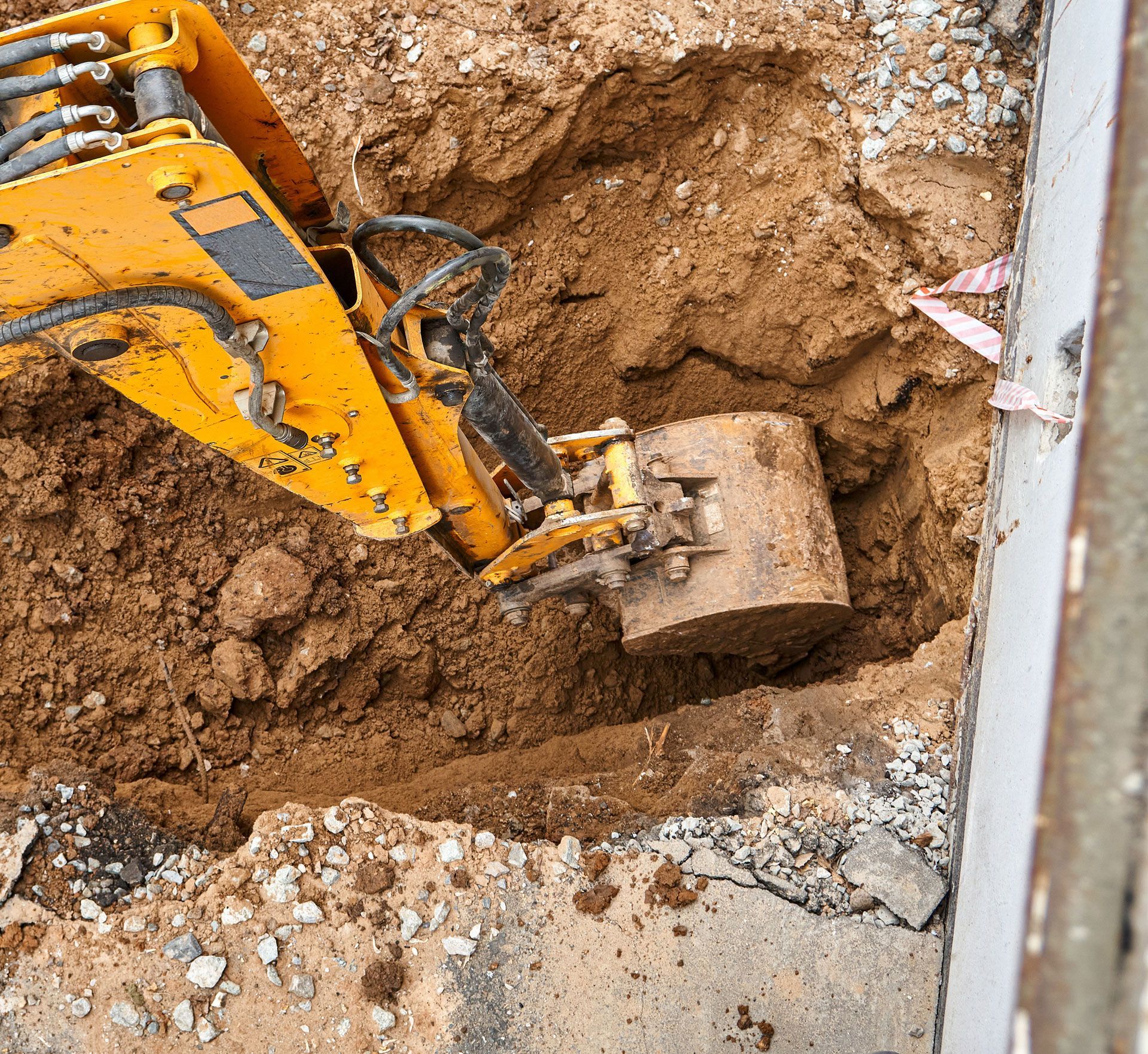 Yellow excavator bucket digging into a muddy trench beside a concrete edge