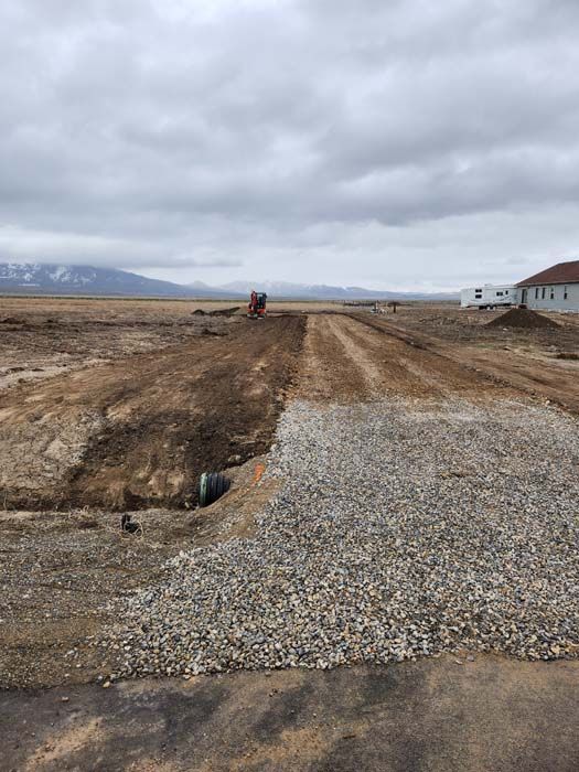 Dirt road under construction with gravel, with mountains in the background.