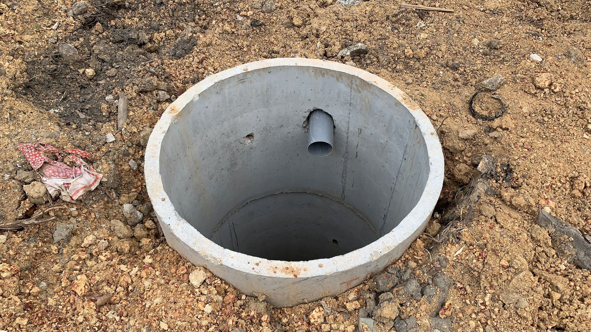 Concrete utility access pit in dirt with a pipe opening inside