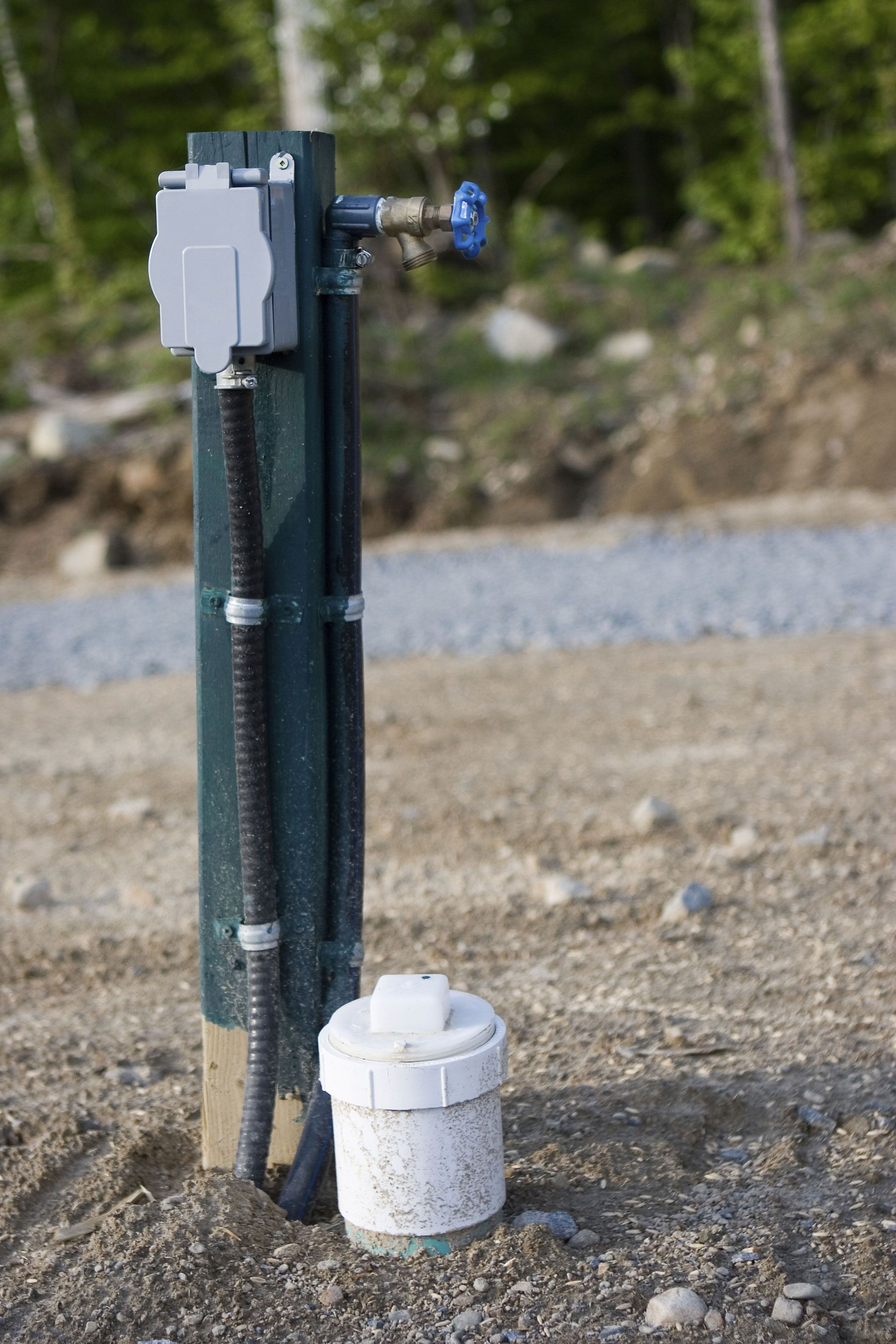 Two black fishing rods with a white bait bucket on gravel outdoors