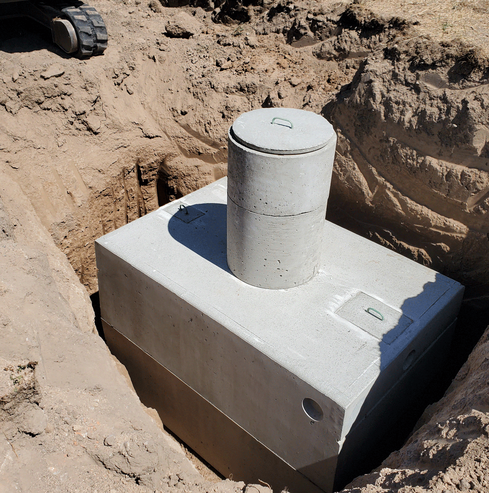 Concrete utility vault with a cylindrical pipe in a sandy excavation site