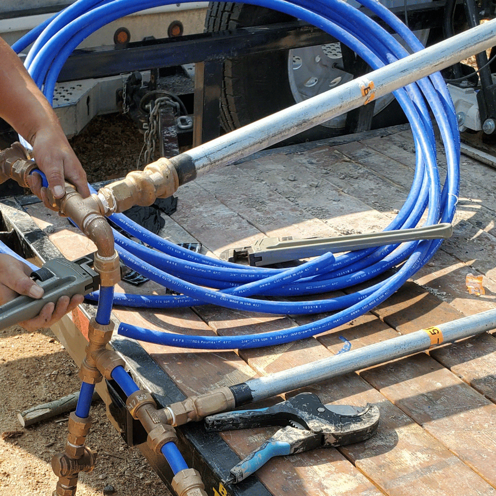 Worker handling blue hoses and metal pipes on a sunlit construction site