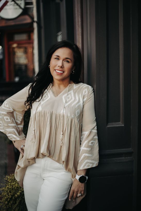 A woman is sitting at a desk with a laptop and a vase of flowers.
