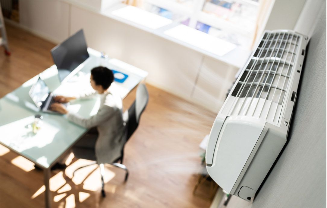 Condizionatore bianco sulla parete, persona che lavora alla scrivania vicino alla finestra.